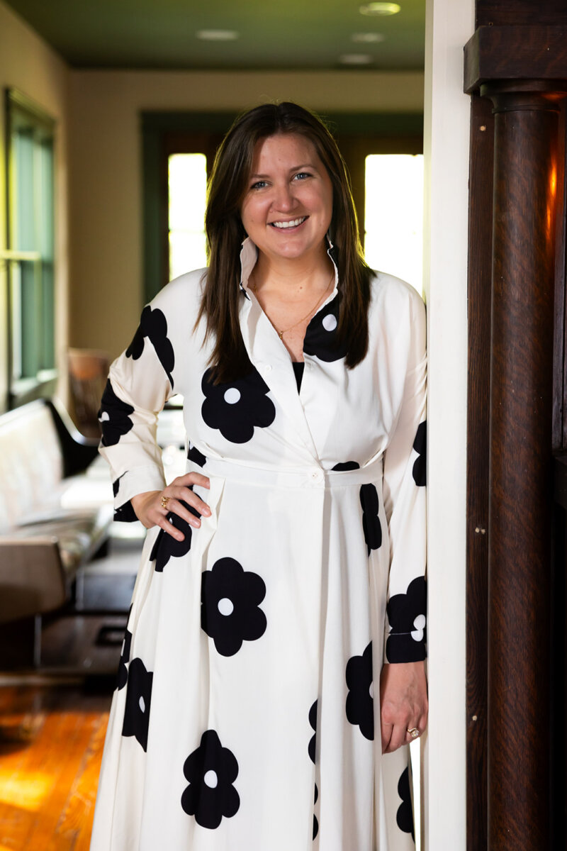Meet the Sommelier Behind Nashville's Newest Wine Bar + Bodega - 7 Lauren Maranto stands indoors, smiling, wearing a long white dress adorned with large black flower patterns.
