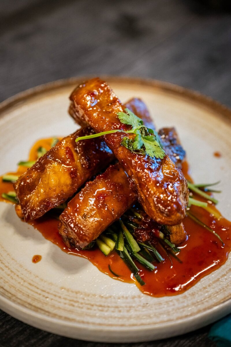 7 New Nashville Restaurants to Try This Month - 7 Three glazed ribs stacked atop julienned vegetables, garnished with cilantro, served on a beige plate with rich sauce—a flavorful highlight among new restaurants.