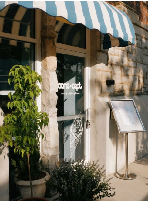 7 New Nashville Restaurants to Try This Month - 3 A storefront with a blue-and-white striped awning, potted plants by the entrance, and a menu display stand outside. The door features an ice cream cone graphic and text.