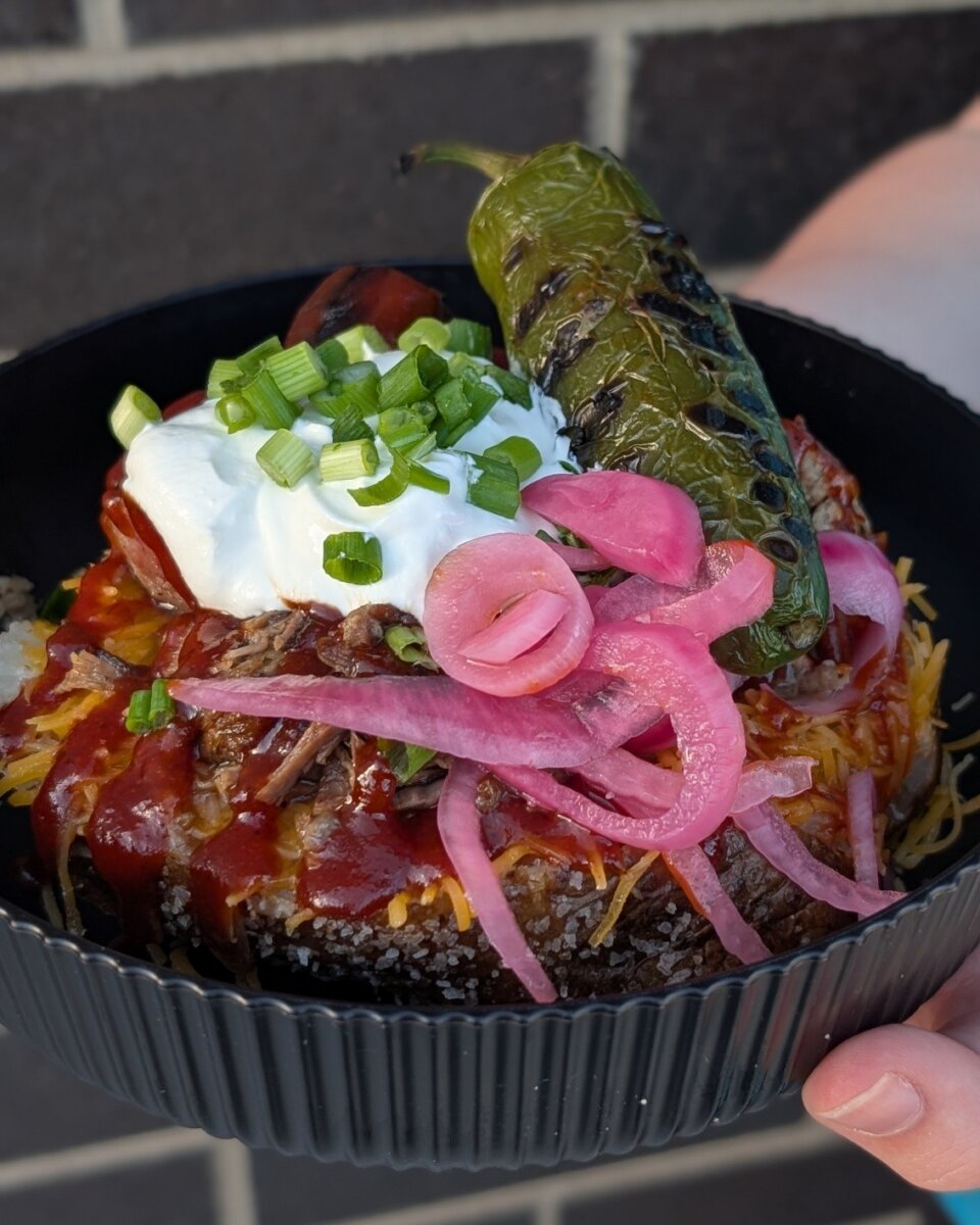 7 New Nashville Restaurants to Try This Month - 8 A black bowl filled with shredded beef, barbecue sauce, grated cheese, pickled onions, sour cream, chopped green onions, and a grilled jalapeño pepper.
