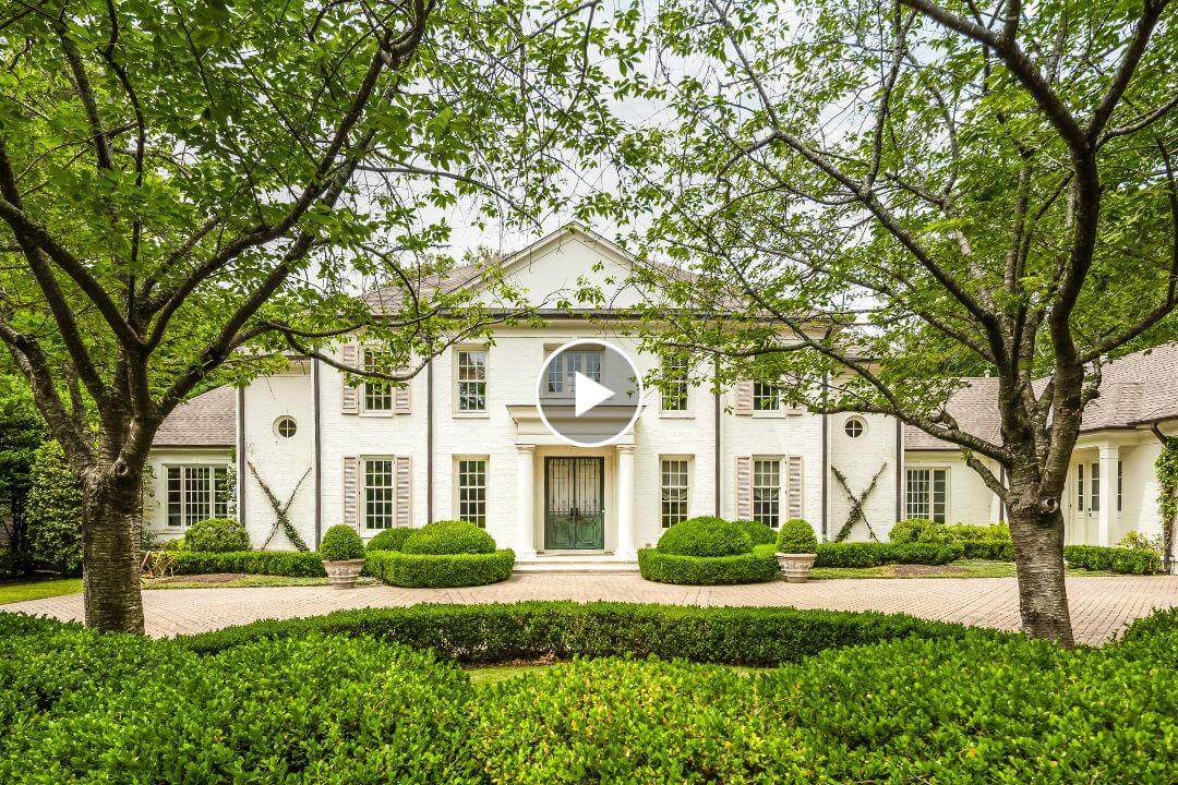 Elegant large white two-story house with columns in Memphis, surrounded by manicured bushes and trees, featuring a circular driveway in front. Located at 4068 Robinwood Cv.