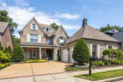 Two-story suburban brick house at 1702 Padington Park Ln, Germantown TN, with attached garage, manicured lawn, shrubs, driveway, sidewalk, and a black mailbox in front under a partly cloudy sky.