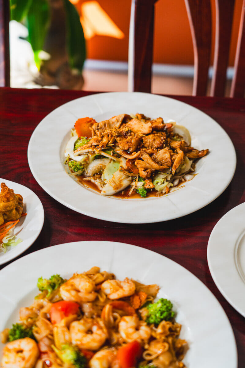 Need a Change of Scenery? Try These Summer Weekend Trips From Nashville - 9 A table with plates of stir-fried chicken and vegetables, shrimp with noodles, and fried dumplings set on a wooden surface—perfect for fueling up before weekend trips from Nashville.