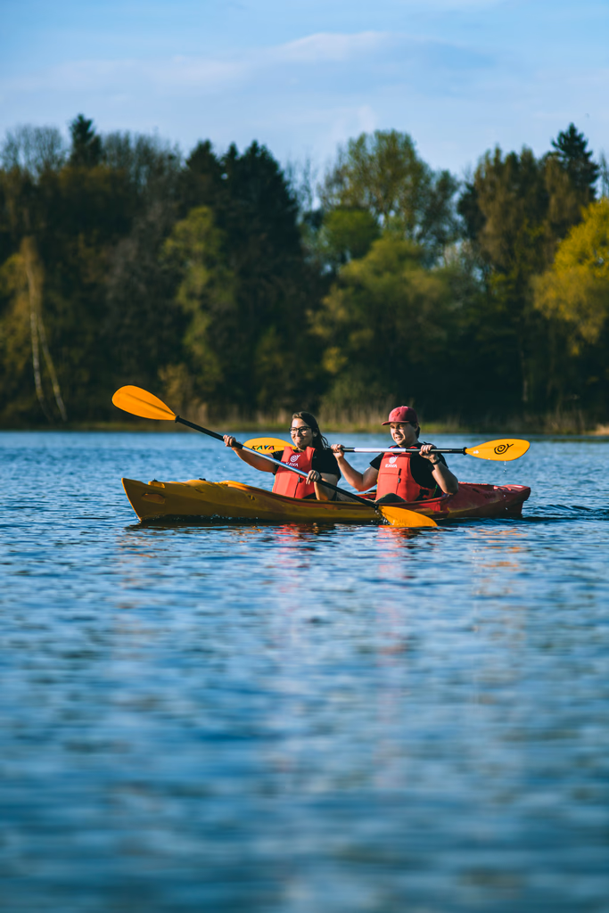 Need a Change of Scenery? Try These Summer Weekend Trips From Nashville - 13 Two people wearing life jackets kayak on a calm lake with trees in the background under a clear sky—an ideal scene for day trips from Nashville.