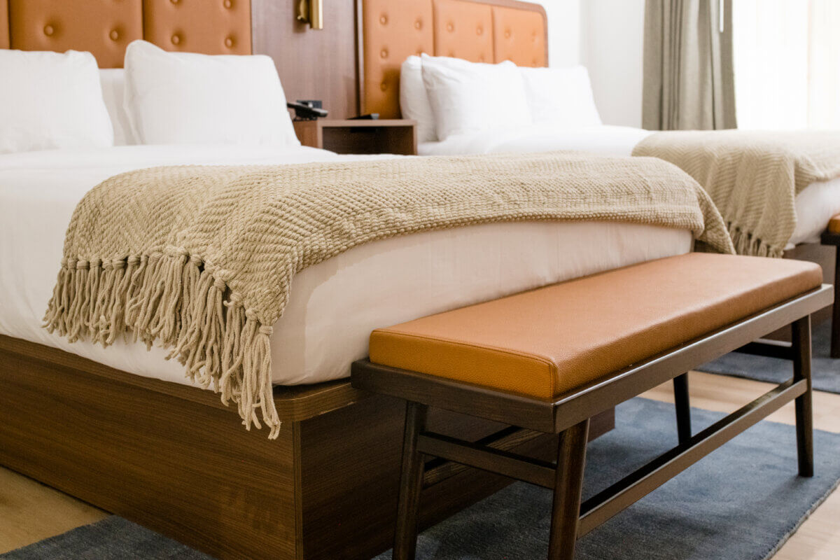 4 New Nashville Boutique Hotels That Should Be on Your Radar - 10 Two neatly made beds with white linens and beige knit throws are positioned side by side, each with a brown leather bench at the foot of the bed in a modern hotel room.