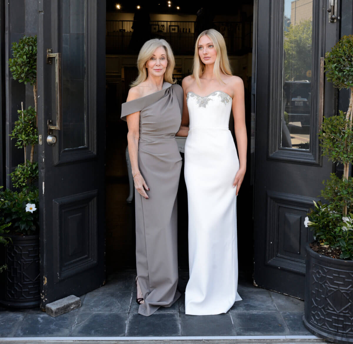 The Event-Season Trends Nashville Boutiques Are Loving Right Now - 5 All Dressed Up, two women stand side by side in formal dresses at the entrance of a building with open double doors and decorative plants.