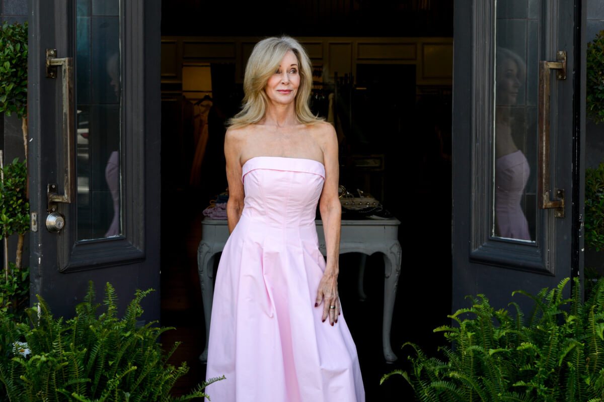 A woman with long blonde hair, Dressed Up in a strapless pink dress, stands in a doorway surrounded by green plants, showcasing her effortless fashion style.