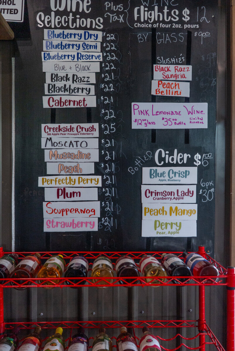 4 Summer Weekend Trips from Atlanta - 8 Menu board displaying various wine, cider, and slushie options with prices, next to a wine rack holding several bottles—perfect for relaxing Atlanta summer weekend trips.