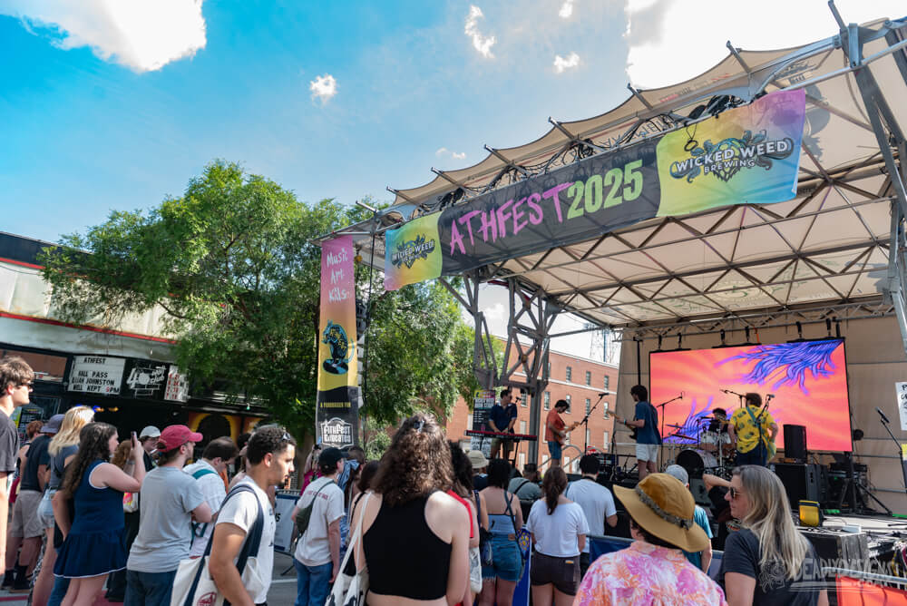 The Best Summer Weekend Getaways in the South - 9 A crowd enjoys a band performing on an outdoor stage at AthFest 2025 under a canopy, with banners and a digital screen—making it a perfect stop for summer weekend trips in the South.