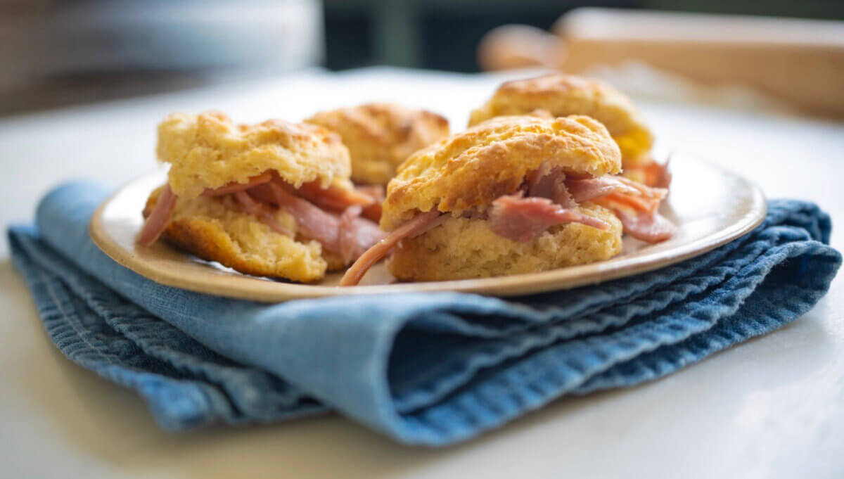 The Best Summer Weekend Getaways in the South - 5 Four ham biscuits are arranged on a plate, which rests on a folded blue cloth—a classic taste of the South, perfect for summer weekend trips.