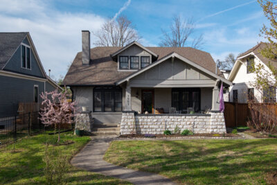 A Craftsman-style house with a stone porch, front steps, and a blooming tree in the yard on a sunny day at 1003 Mansfield Ave, highlighting charming Nashville TN real estate.