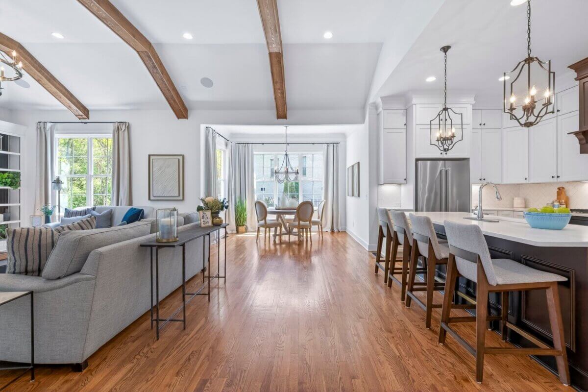 Open-concept living space at 2708 Eglington Terrace features wooden floors, exposed ceiling beams, a modern kitchen with island seating, a dining area, and a furnished living room with large windows in Franklin, TN.