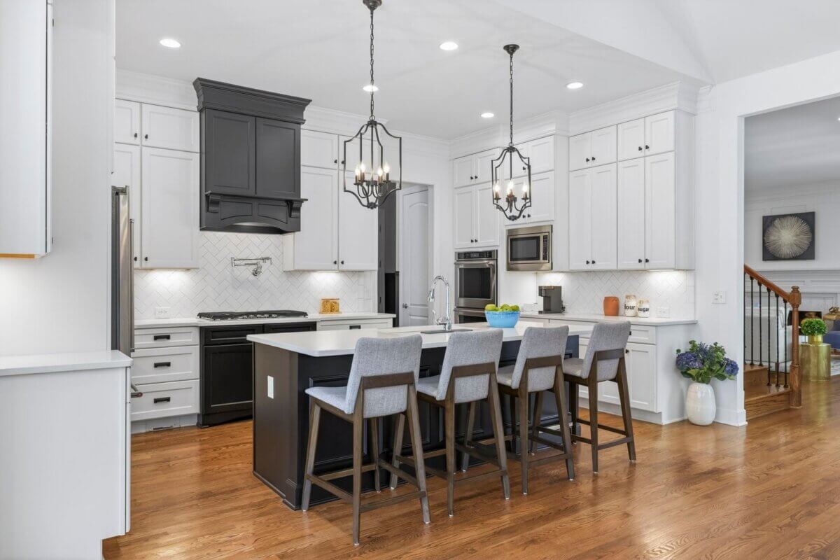 Modern kitchen in Franklin TN featuring white cabinets, a black island with four gray barstools, stainless steel appliances, pendant lights, and hardwood floors on Eglington Terrace at 2708.