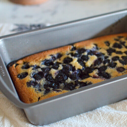 RECIPE: Easy Blueberry Buckle - 4 A rectangular metal baking pan holds a freshly baked blueberry cake resting on a light-colored cloth.