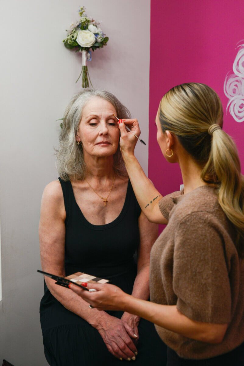 The Event-Season Trends Nashville Boutiques Are Loving Right Now - 14 A makeup artist applies eyeshadow to an older woman sitting with her eyes closed in a room with pink and white walls.