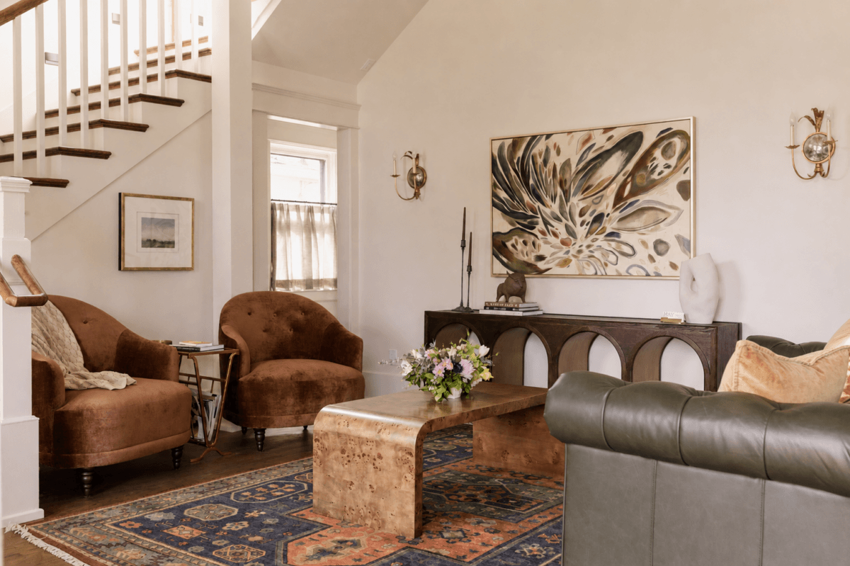 4 New Nashville Boutique Hotels That Should Be on Your Radar - 13 A cozy living room with brown velvet chairs, a green leather sofa, a wooden coffee table, an abstract painting, and a colorful rug under a staircase.
