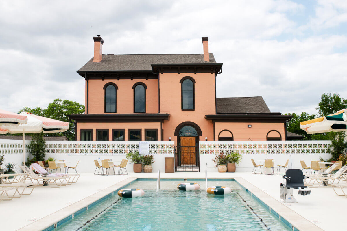 4 New Nashville Boutique Hotels That Should Be on Your Radar - 11 A rectangular outdoor pool with floating lane dividers is surrounded by lounge chairs and umbrellas in front of a two-story peach-colored house with arched windows.