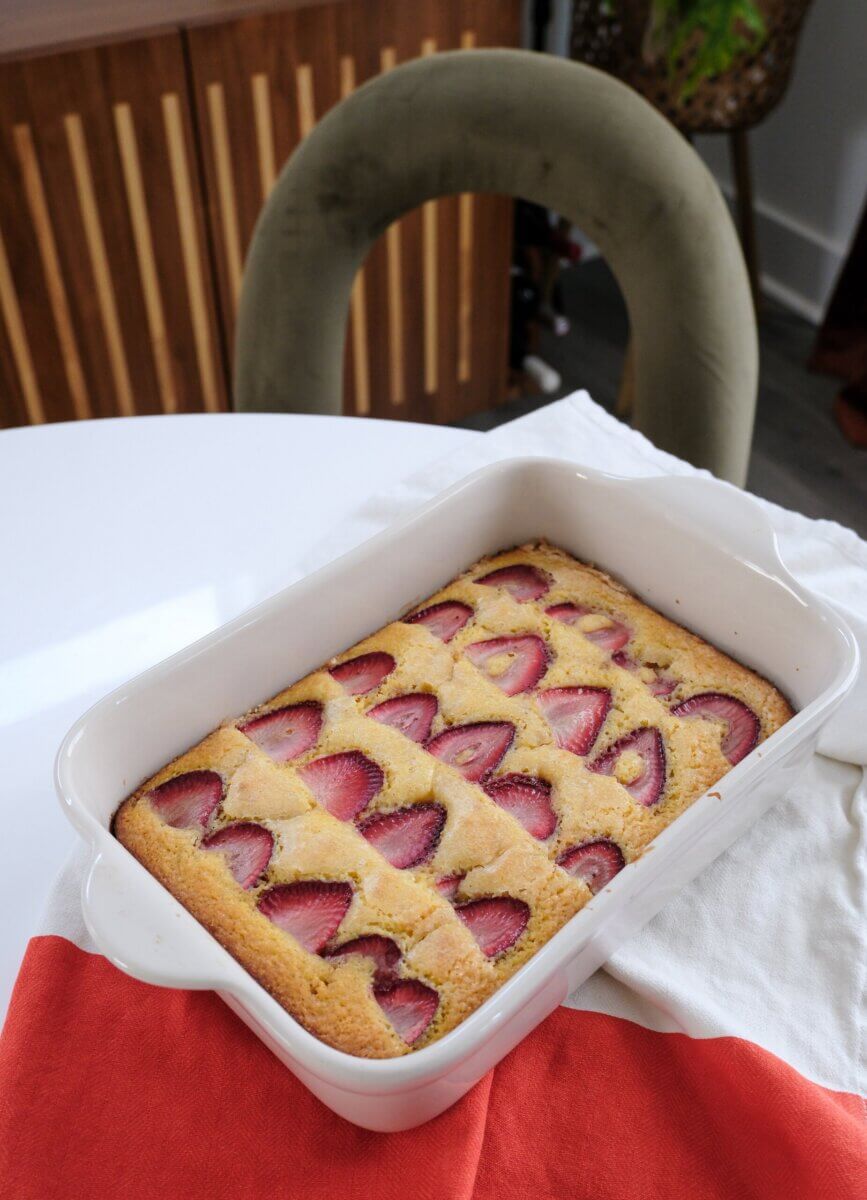 Two Summery Snack Cakes, Perfect for Picnics & Potlucks - 3 A rectangular baking dish filled with a golden-brown cake topped with rows of sliced strawberries sits on a white table with red and white napkins.