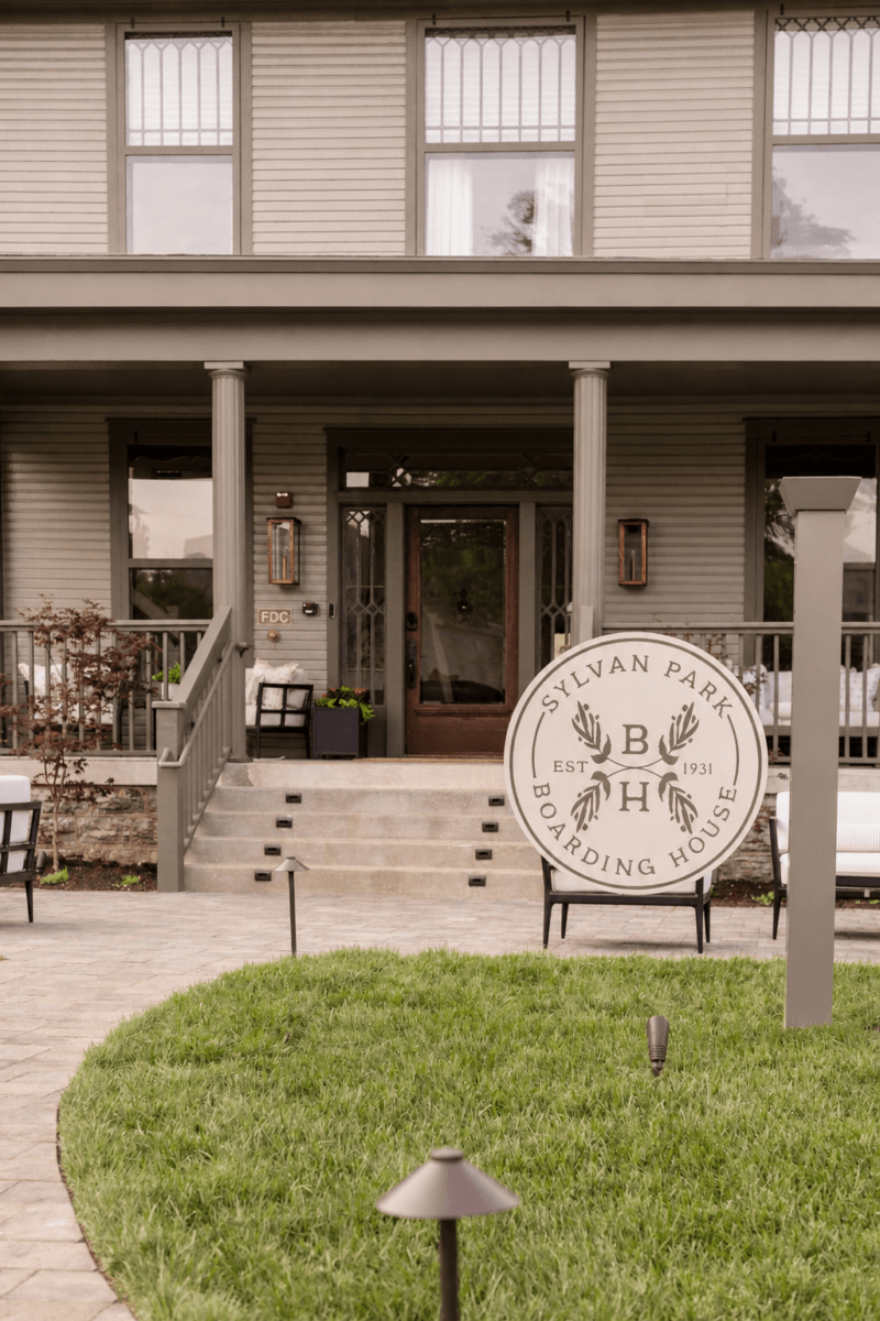 4 New Nashville Boutique Hotels That Should Be on Your Radar - 12 A large sign reading "Sylvan Park Boarding House" stands in front of a gray, two-story building with a porch and steps leading to the entrance.