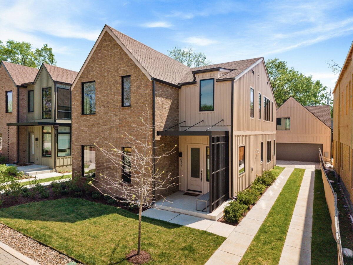 Two modern suburban houses with brick and siding exteriors at 627 Richmond Bnd, Nashville TN, featuring a tree in the front yard and a driveway leading to a detached garage under a blue sky.