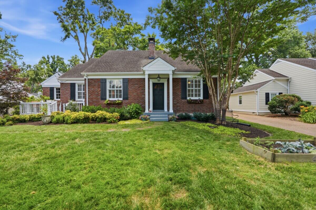 A brick house with black shutters and white trim sits behind a green lawn at 3008 Natchez Trce, Nashville, surrounded by landscaping and trees, with a driveway and garage visible to the right.