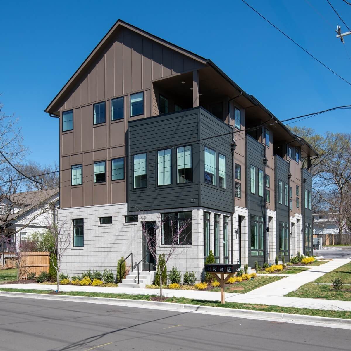 Modern three-story townhouse building on Lischey Ave, Nashville TN, featuring large windows, balconies, and landscaped surroundings on a sunny day.