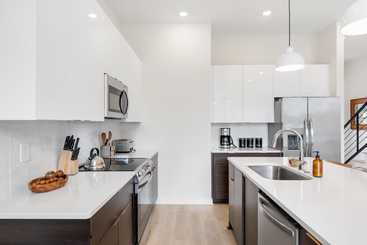 Modern kitchen at 1233 Lischey Ave in Nashville featuring white cabinets, stainless steel appliances, a double sink, countertop appliances, and light wood flooring under bright overhead lighting.