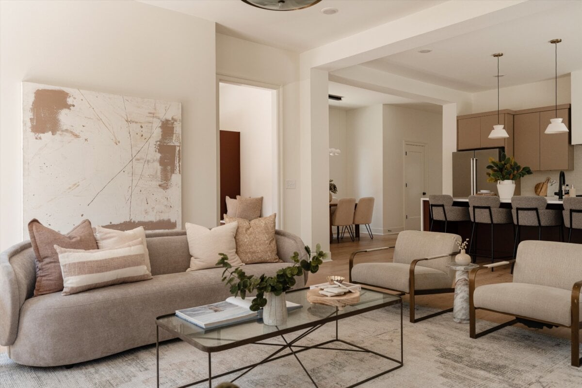 Modern living room with neutral tones, featuring a beige sofa, two armchairs, a glass coffee table, abstract wall art, and an open kitchen in the background—perfect for comfortable living at 627 Richmond Bnd in Nashville.