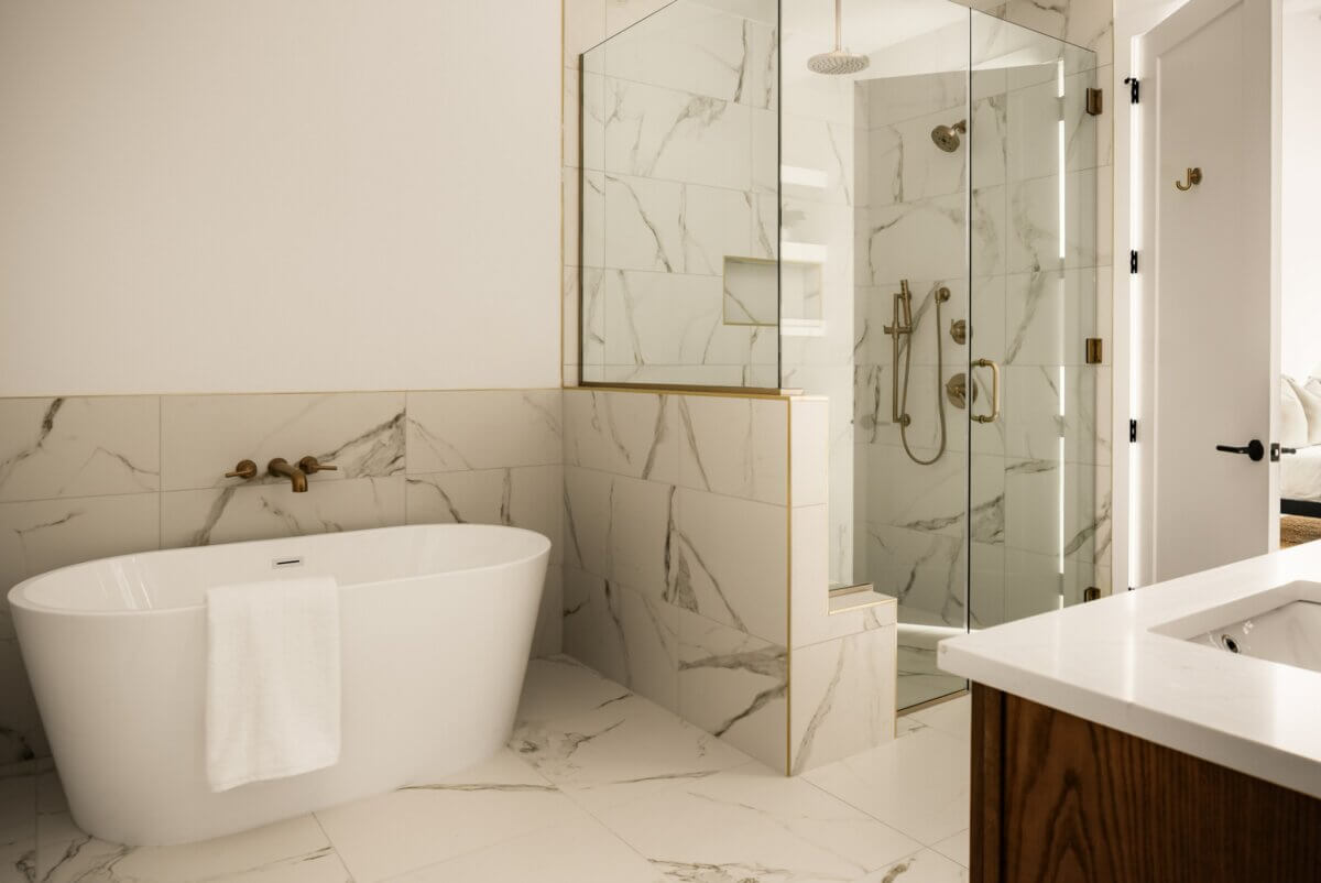 Modern Nashville bathroom with white marble tile, a freestanding bathtub with towel, glass-enclosed shower, and a partial view of a vanity with wood base at 321 321 31st Ave N.