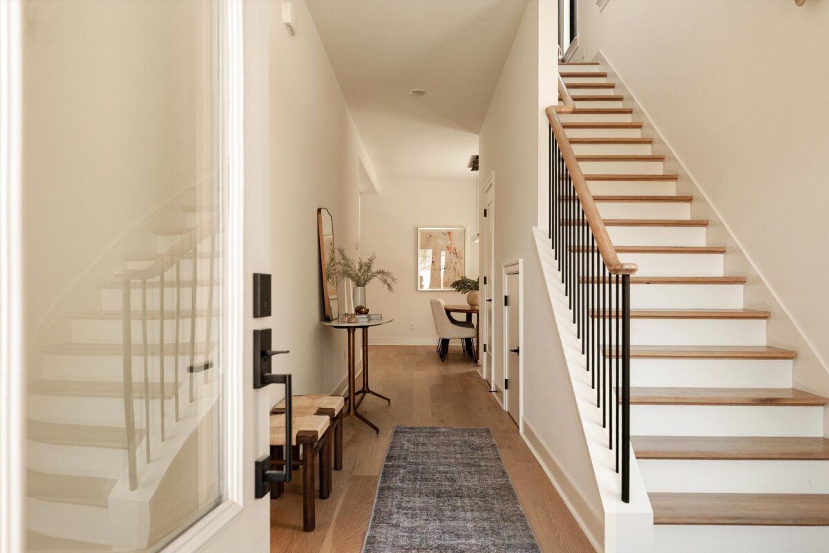 A bright entryway at 627 Richmond Bnd in Nashville features wooden stairs, black handrails, a blue rug, a narrow console table, a mirror, and two benches along the wall.