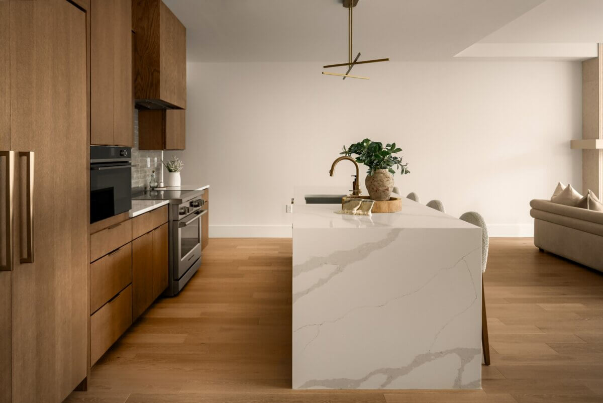 Modern kitchen at 321 31st Ave N, Nashville TN, with wood cabinets, stainless steel appliances, a white marble island, gold faucet, and minimalist decor. Light wood flooring and neutral tones throughout.