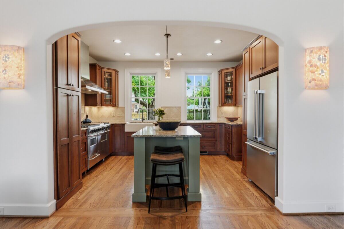 Modern kitchen in Nashville TN with wooden cabinets, stainless steel appliances, a central island with two stools, pendant lighting, and large windows filling the space with natural light—perfect for real estate at 3008 New Natchez Trce.