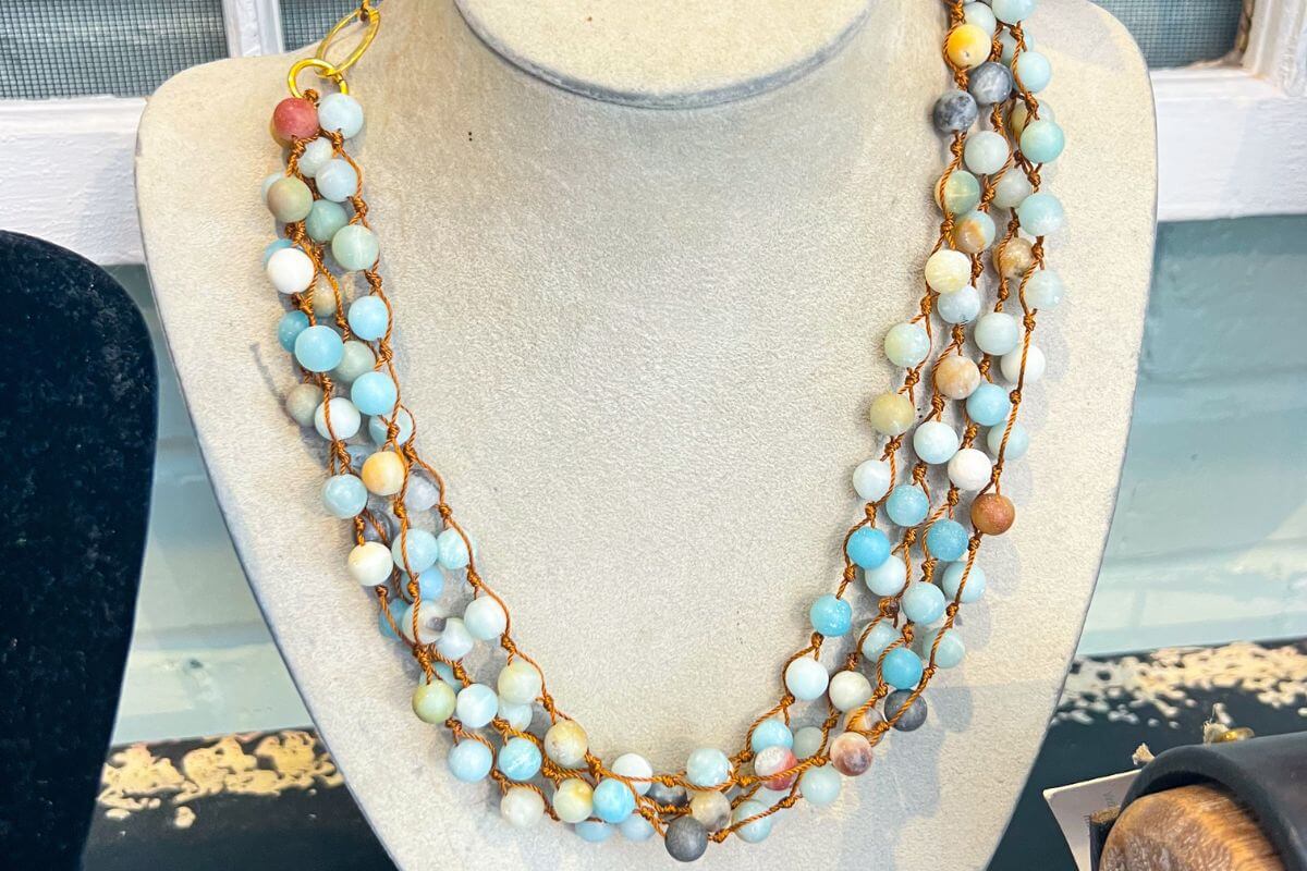A multi-strand necklace made of round, pastel-colored beads displayed on a jewelry bust.