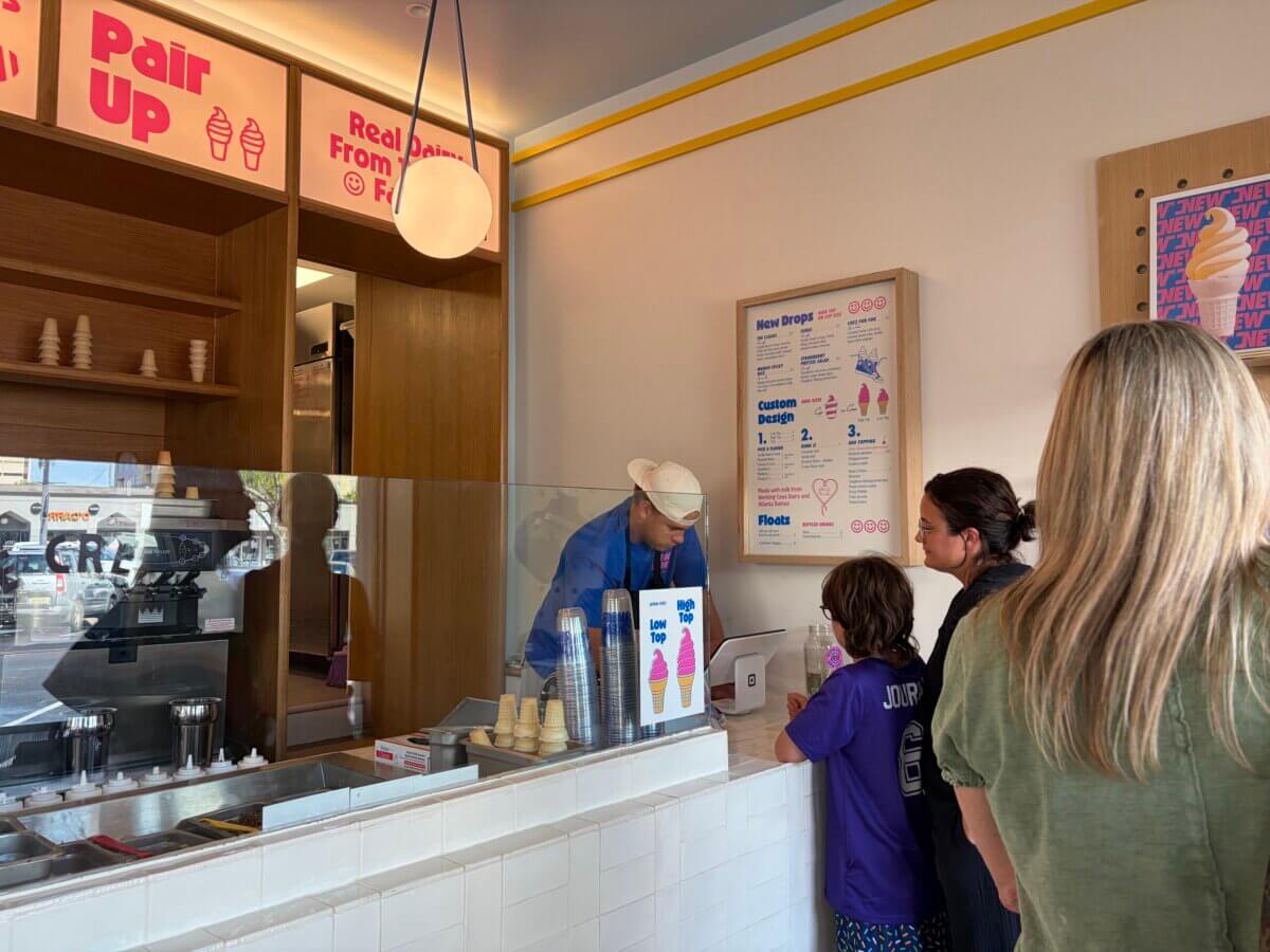 Scoops of Nostalgia: Why Everyone is Lining Up for New Shoes Soft Serve - 3 Customers stand at the New Shoes Soft Serve counter in Homewood as an employee in a blue shirt and white hat serves them. Menus and cones are visible behind the counter.
