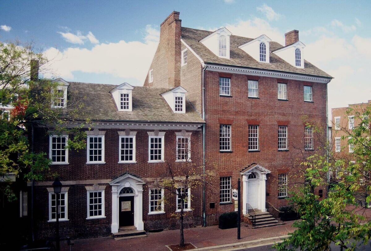How to Spend a Perfect Weekend in Old Town Alexandria, VA - 7 Two historic brick buildings with white-trimmed windows and doors sit on a tree-lined street in Old Town Alexandria, VA, under a partly cloudy skyβa charming scene for a weekend stroll.