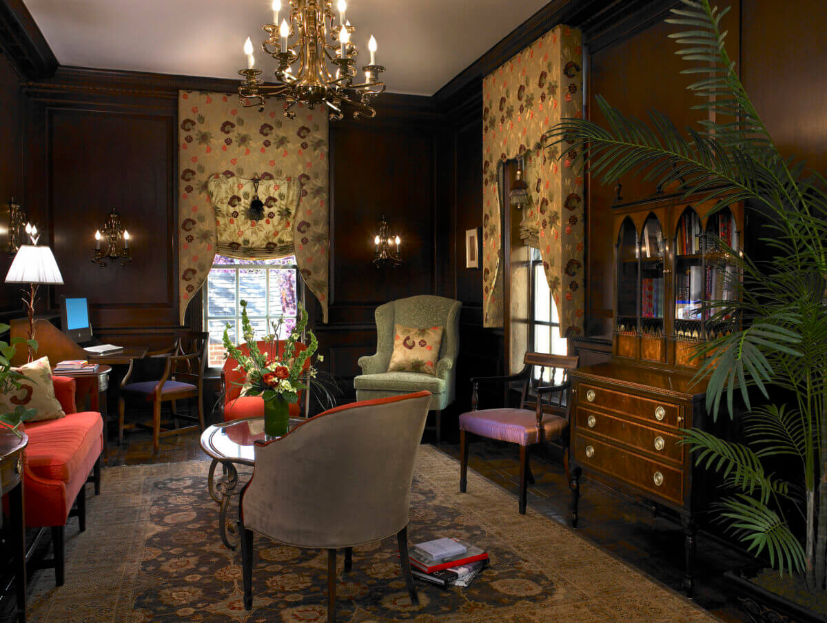 How to Spend a Perfect Weekend in Old Town Alexandria, VA - 3 Traditional sitting room with dark wood paneling, patterned wallpaper, antique furniture, floral arrangements, and a chandelierβevoking the timeless charm of Old Town Alexandria, VAβwith a desk, armchairs, and a large rug.
