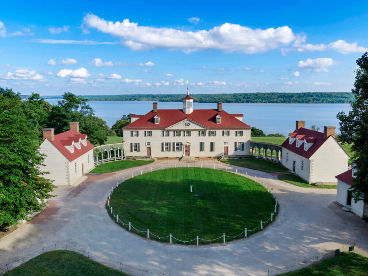 How to Spend a Perfect Weekend in Old Town Alexandria, VA - 4 A large historic mansion with white walls and red roofs overlooks a river in Old Town Alexandria, flanked by two smaller buildings, and surrounded by a circular driveway and manicured lawnβperfect for a weekend stroll.