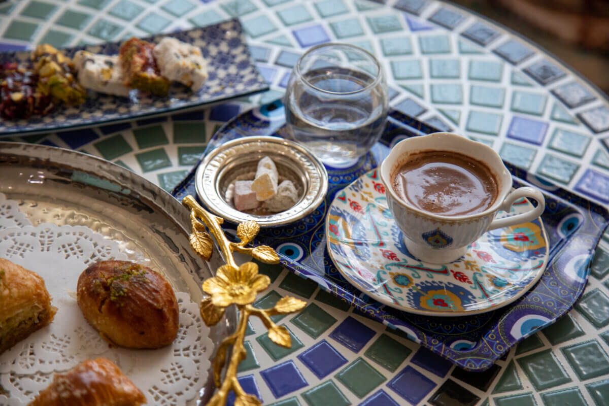 How to Spend a Perfect Weekend in Old Town Alexandria, VA - 6 A cup of Turkish coffee on a patterned saucer, a glass of water, Turkish delight, and assorted pastries grace a mosaic-tiled tableβperfect for a relaxing weekend in Old Town Alexandria, VA.