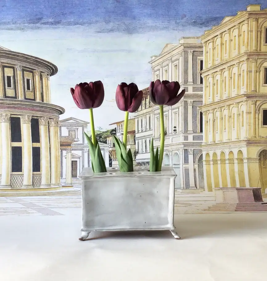 17 Luxurious Birmingham FINDS: Polished Summer Style, Artful Decor & Everyday Luxuries - 13 Three dark purple tulips in a rectangular white vase are placed in front of a backdrop featuring luxurious classical European architecture, evoking the elegance of a Birmingham summer.