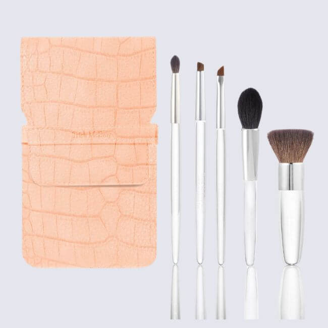 17 Luxurious Birmingham FINDS: Polished Summer Style, Artful Decor & Everyday Luxuries - 18 A peach textured brush pouch is shown next to five silver-handled makeup brushes of various sizes and shapes on a light gray background—perfect for adding a touch of luxurious Birmingham style to your beauty routine.