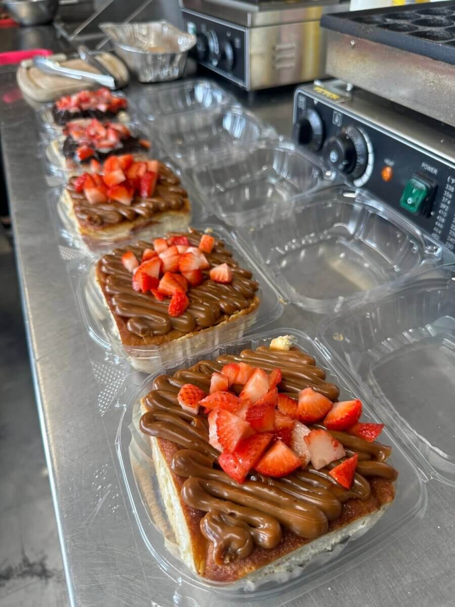 11 New Birmingham Restaurants to Try This Month - 7 Four pastries topped with chocolate spread and sliced strawberries are arranged in clear plastic containers on a stainless steel countertop next to kitchen equipment—a delightful treat you might find at some of the new restaurants in Birmingham.