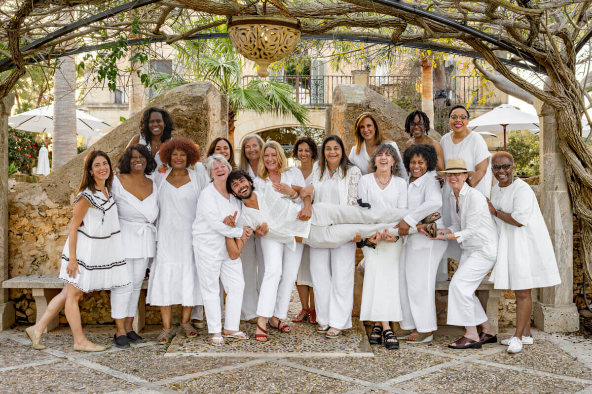 A group of people dressed in white pose outdoors in Birmingham, smiling, with one person being playfully held horizontally by others.