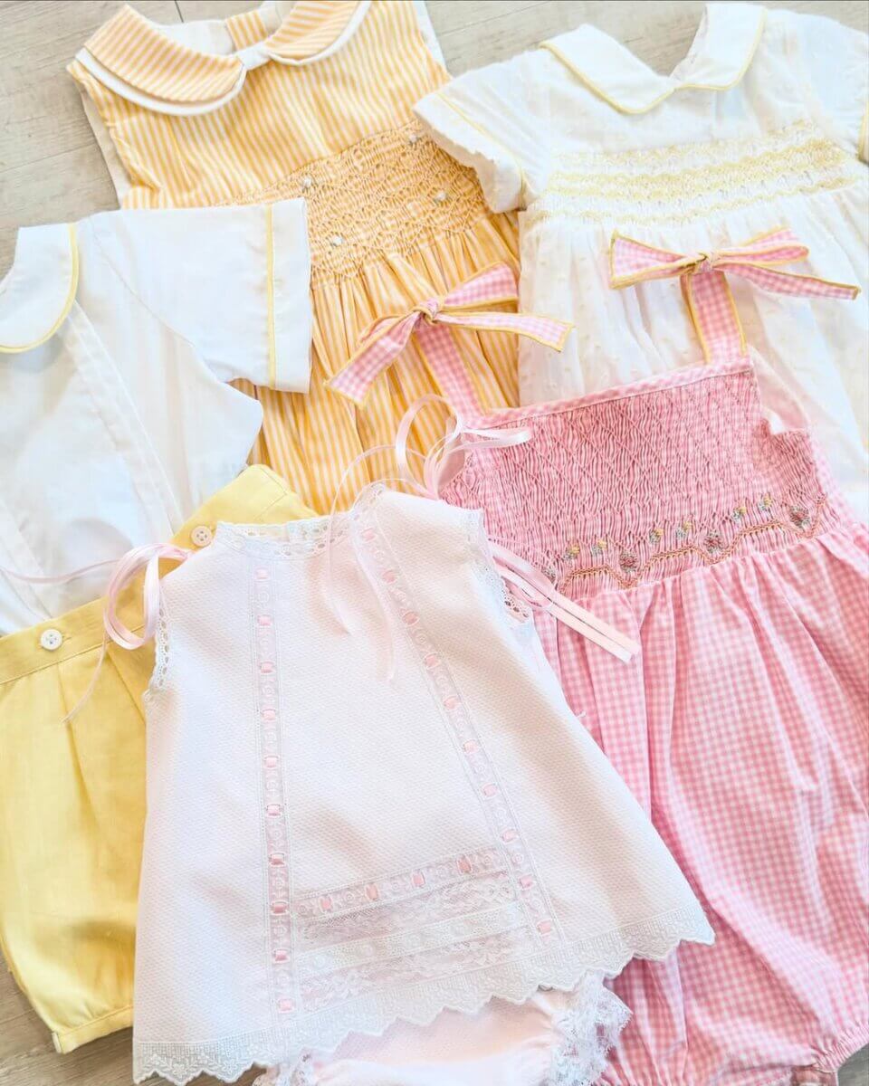 8 Birmingham Children's Boutiques for Every Age - 3 A selection of pastel-colored baby clothes featuring dresses and rompers in pink, yellow, and white with lace, bows, and smocked details from Children's Edit.