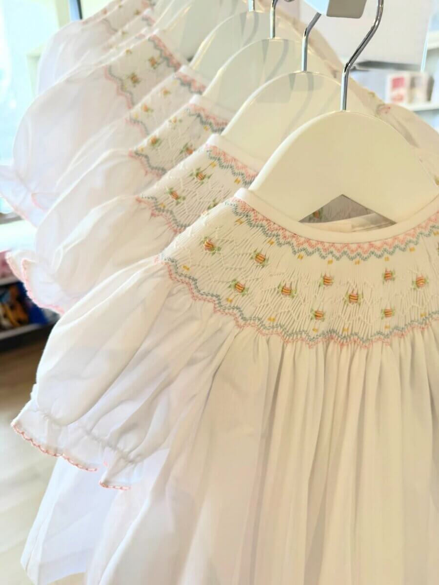 8 Birmingham Children's Boutiques for Every Age - 8 Several white smocked baby dresses with pink and yellow embroidered details hang on white hangers in a row at Dear Emmaline.