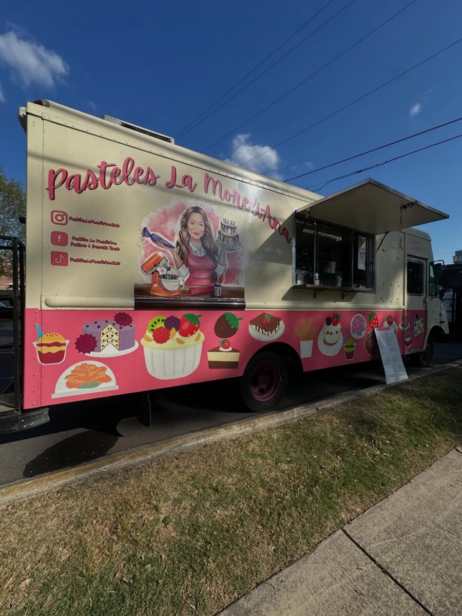 Meet the Internet Star Behind BHAM’s FIRST Mexican Mobile Bakery! - 5 A Mexican Mobile Bakery food truck labeled "Pasteles La Moni Ana," decorated with cakes and a woman holding desserts, is parked on a BHAM street with the service window open.
