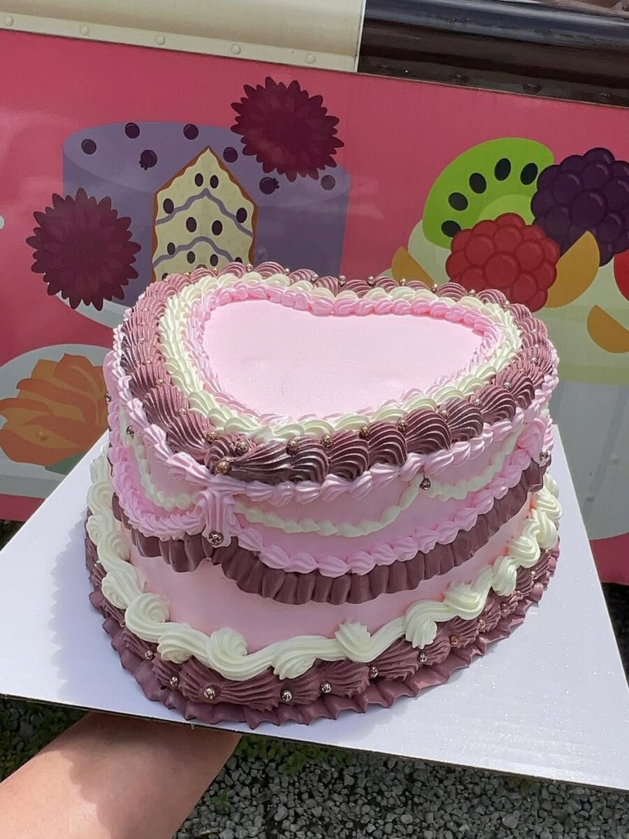 Meet the Internet Star Behind BHAM’s FIRST Mexican Mobile Bakery! - 8 A heart-shaped cake with pink, purple, and white piped frosting details from Mexican Mobile Bakery, displayed on a white board against a colorful illustrated background.