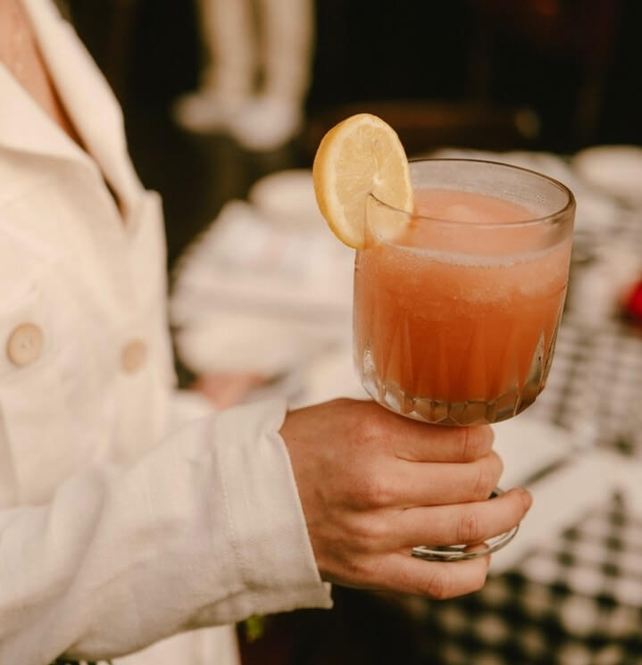 10 Frozen Cocktails to Try in BHAM This Summer - 9 A person in a light-colored jacket holds a glass of pink Frozen sangria garnished with a lemon slice from El Royale Cafe.