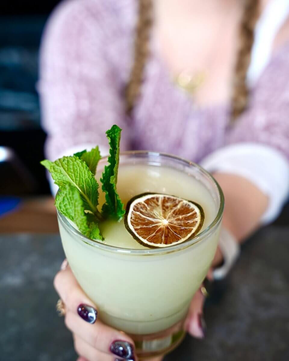 10 Frozen Cocktails to Try in BHAM This Summer - 4 A person holding a frozen mojito cocktail, garnished with a dried lime slice and fresh mint leaves from Social Taco.