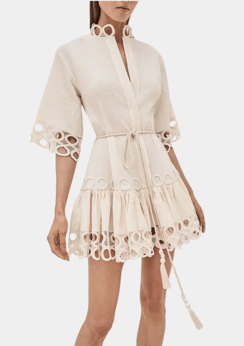 17 Luxurious Birmingham FINDS: Polished Summer Style, Artful Decor & Everyday Luxuries - 3 A woman wears a cream-colored, textured mini dress with a rope belt, ruffled hem, and circular cutout details on the sleeves, collar, and skirt—one of this season’s must-have summer finds in luxurious Birmingham style.