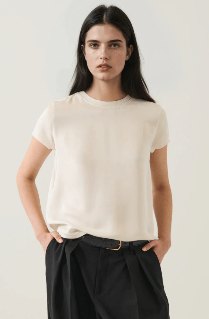 17 Luxurious Birmingham FINDS: Polished Summer Style, Artful Decor & Everyday Luxuries - 6 A woman with long dark hair wears a luxurious, short-sleeved cream blouse tucked into high-waisted black trousers with a belt, standing against a plain light background—perfect for summer days in Birmingham.